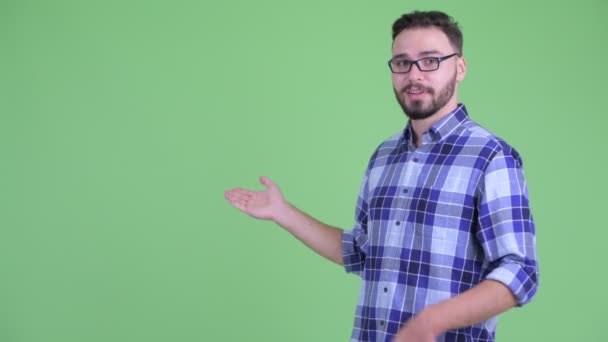 Boldog ifjú szakállas csípő ember beszél, miközben bemutatja a hátsó — Stock videók
