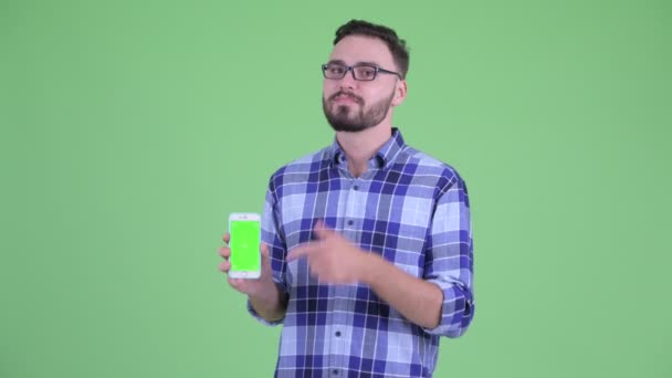 Feliz joven barbudo hipster hombre mostrando el teléfono y dando pulgares hacia arriba — Vídeos de Stock