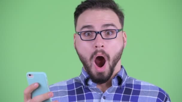 Gelukkig jong bebaarde hipster man met behulp van telefoon en kijken verrast — Stockvideo