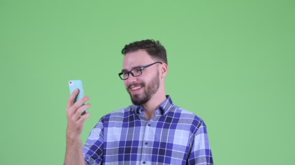 Gezicht van Happy Young bebaarde hipster man met behulp van de telefoon en op zoek verrast — Stockvideo