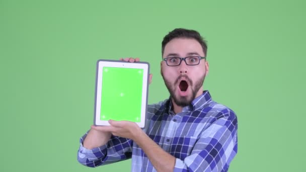 Feliz joven barbudo hipster hombre mostrando tableta digital y mirando sorprendido — Vídeos de Stock