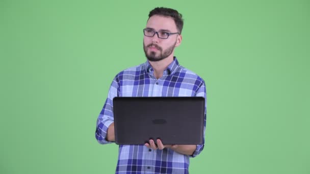 Ευτυχισμένος νέος γενειοφόρος hipster άνθρωπος σκέφτεται κατά τη χρήση laptop — Αρχείο Βίντεο