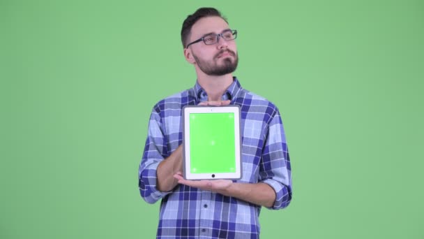 Glücklicher junger bärtiger Hipster-Mann denkt beim Vorzeigen digitaler Tablets — Stockvideo
