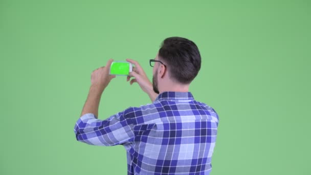 Вид спереду молодого бородатого хіпстера фотографує з телефоном — стокове відео