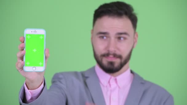 Gezicht van Happy Young bebaarde zakenman toont telefoon en geven duimen omhoog — Stockvideo