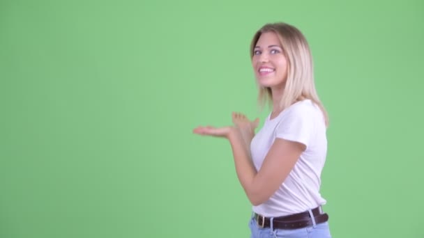 Happy young beautiful blonde woman showing to the back and looking excited — Stock Video
