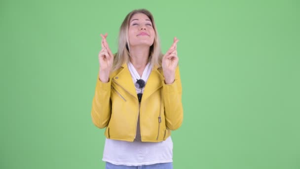 Happy young rebellious blonde woman wishing with fingers crossed — Stock Video