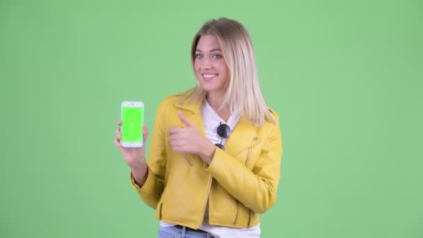 Happy young rebellious blonde woman showing phone and giving thumbs up — Stock Video