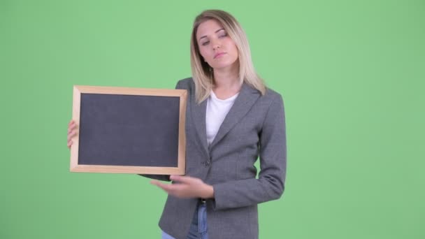 Beklemtoonde jonge blonde zakenvrouw die Blackboard vasthoudt en duimen naar beneden geeft — Stockvideo
