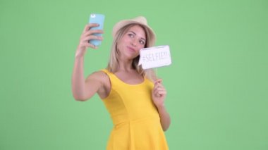 Mutlu genç sarışın turist kadın kağıt işareti ile selfie alarak