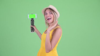 Mutlu genç sarışın turist kadın vlogging ve gösteren telefon