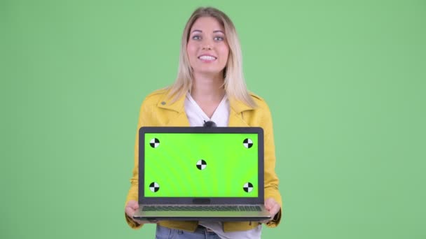 Щаслива молода бунтівлива блондинка говорить, показуючи ноутбук — стокове відео