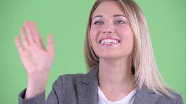 Gezicht van gelukkig jonge mooie blonde zakenvrouw zwaaiende hand — Stockvideo