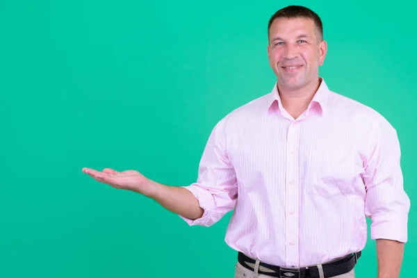 何かを示すピンクのシャツを持つ幸せな成熟したマッチョビジネスマン — ストック写真