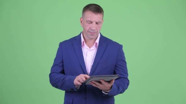 Зрелый мачо бизнесмен в костюме мышления при использовании цифрового планшета — стоковое видео