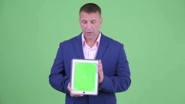 Mature macho homme d'affaires en costume parler tout en montrant tablette numérique — Video