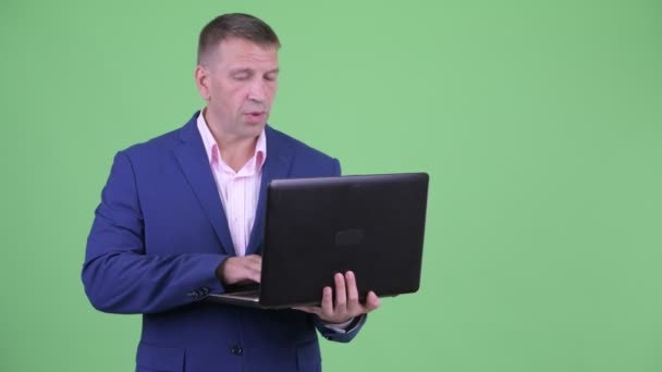 Olgun maço işadamı dizüstü bilgisayar kullanırken konuşurken takım elbiseli — Stok video