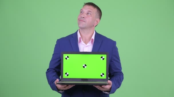 Счастливый зрелый мачо бизнесмен в костюме думает, показывая ноутбук — стоковое видео
