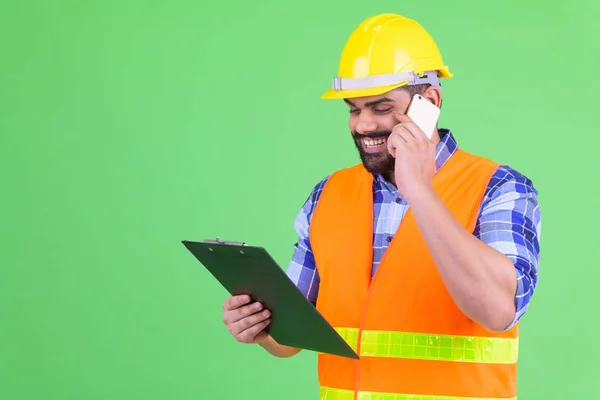 Jovens felizes com sobrepeso barbudo indiano trabalhador da construção civil lendo na área de transferência e falando ao telefone — Fotografia de Stock