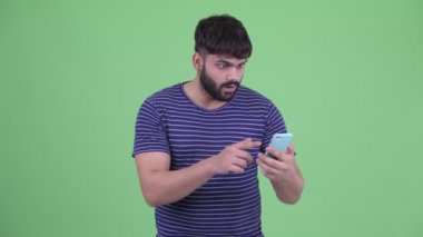 Mutlu genç kilolu sakallı Hintli adam telefon kullanarak ve iyi haber alıyorum
