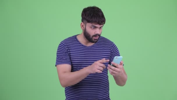 幸せな若い太りすぎのひげを生やしたインド人男性は、携帯電話を使用して、良いニュースを得る — ストック動画