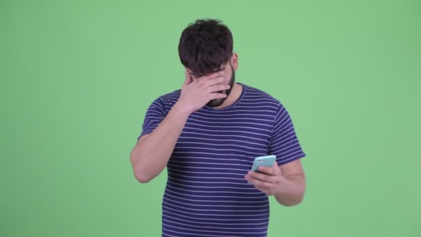 Стресс молодой толстый бородатый индиец с помощью телефона и получать плохие новости — стоковое видео