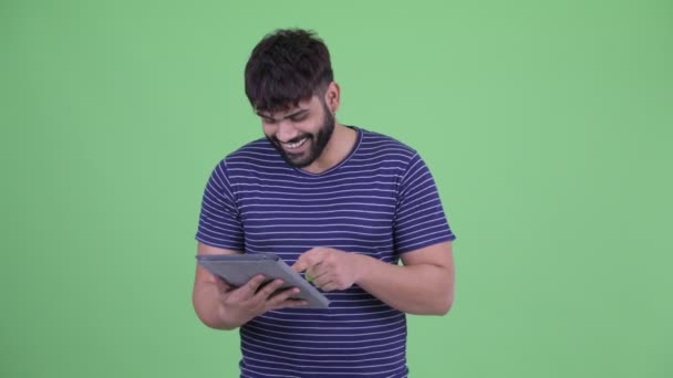 Счастливый молодой толстый бородатый индиец, использующий цифровой планшет — стоковое видео