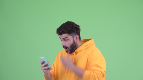 Feliz joven con sobrepeso barbudo hombre indio usando el teléfono y mirando sorprendido — Vídeo de stock