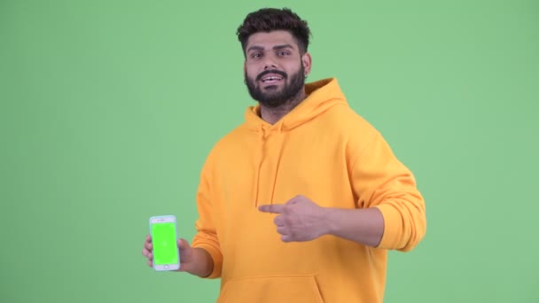 Felice giovane barbuto sovrappeso uomo indiano mostrando telefono e dando pollici in su — Video Stock