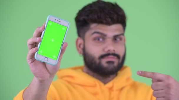 Πρόσωπο του ευτυχισμένο νεαρό υπέρβαρο με γένια Ινδός άνθρωπος δείχνει το τηλέφωνο και δίνοντας αντίχειρες επάνω — Αρχείο Βίντεο