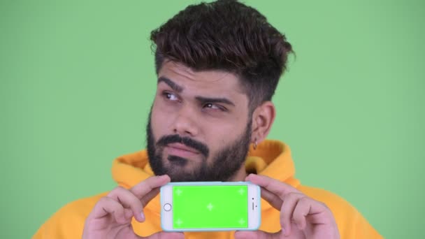 Gezicht van Happy Young overgewicht bebaarde Indiase man denken terwijl het tonen van telefoon — Stockvideo