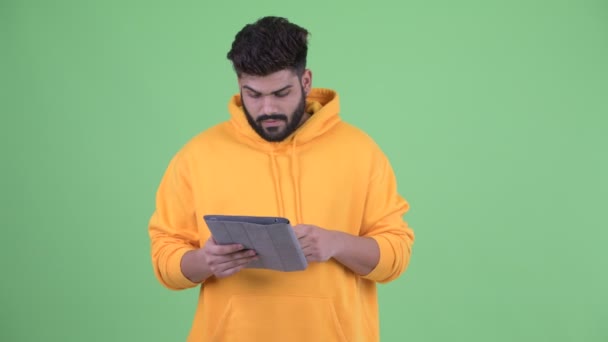 Feliz joven con sobrepeso barbudo hombre indio pensando mientras se utiliza la tableta digital — Vídeos de Stock