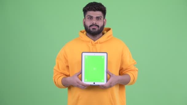 Счастливый молодой толстый бородатый индиец говорит, показывая цифровой планшет — стоковое видео