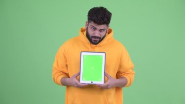 Mutlu genç kilolu sakallı Hintli adam dijital tablet gösterirken düşünme