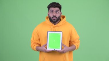 Mutlu genç kilolu sakallı Hintli adam dijital tablet gösteren ve şaşırmış görünümlü