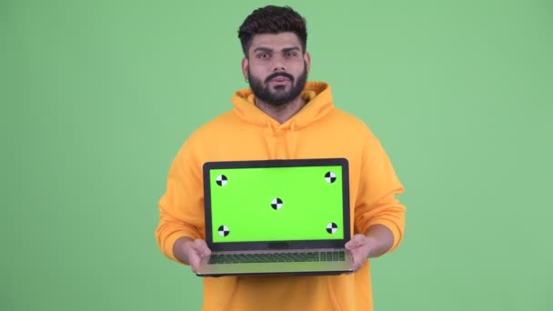 Szczęśliwy młody nadwaga Brodaty Indyjski człowiek mówi podczas pokazując laptop — Wideo stockowe