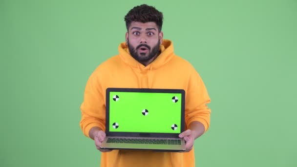 Szczęśliwy młody nadwaga Brodaty Indyjski człowiek pokazując laptop i patrząc zaskoczony — Wideo stockowe