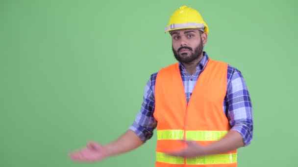 Estressado jovem com sobrepeso barbudo indiano trabalhador da construção mostrando algo — Vídeo de Stock