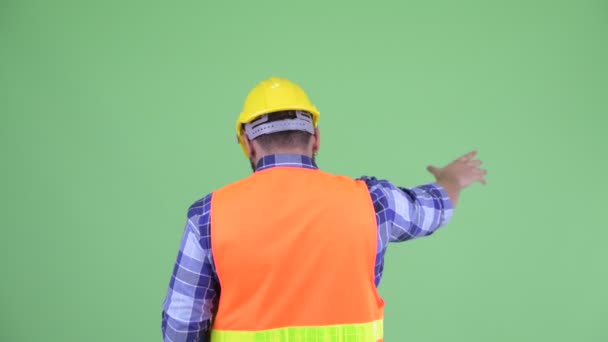 Vista trasera de joven sobrepeso barbudo hombre indio trabajador de la construcción señalando el dedo — Vídeo de stock