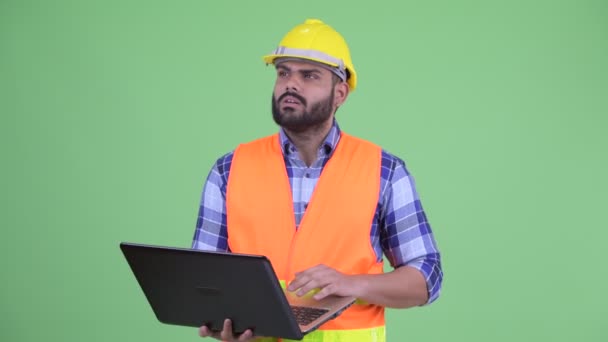 Feliz joven sobrepeso barbudo hombre indio trabajador de la construcción pensando mientras se utiliza el ordenador portátil — Vídeo de stock