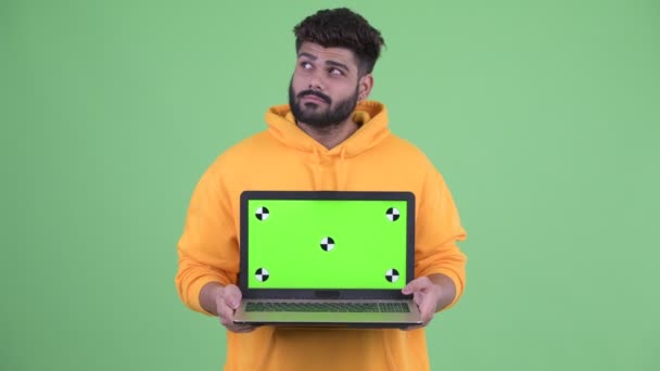 Щаслива молода надмірна вага бородатий індійський чоловік думає, показуючи ноутбук — стокове відео