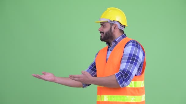 Feliz joven con sobrepeso barbudo trabajador de la construcción hombre indio mostrando algo — Vídeos de Stock