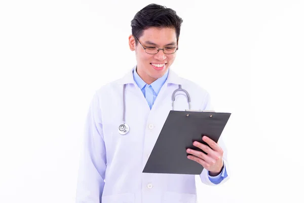 Happy young handsome Asian man doctor reading on clipboard — Stock Photo, Image