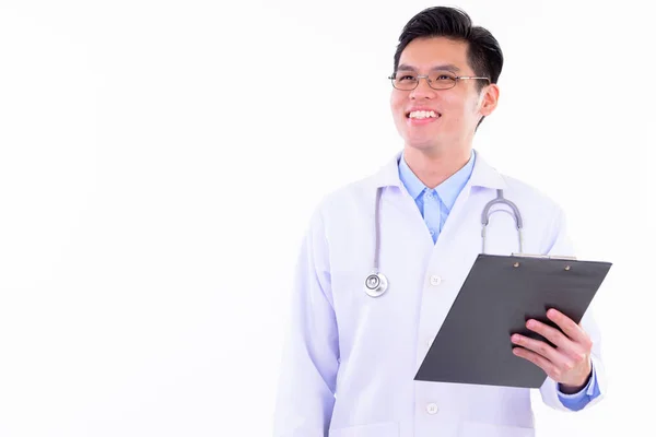 Feliz joven guapo asiático hombre médico pensando mientras sostiene portapapeles —  Fotos de Stock