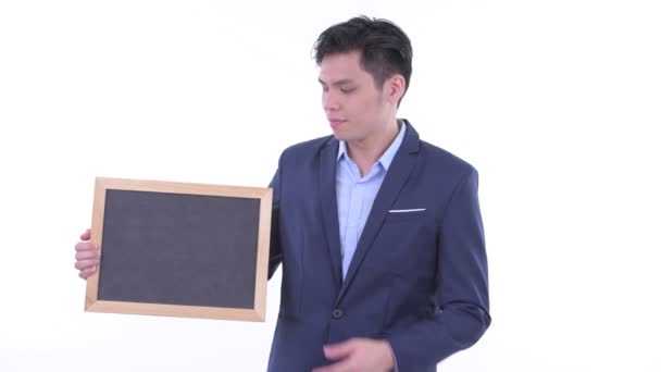Stressed jovem empresário asiático segurando quadro negro e dando polegares para baixo — Vídeo de Stock