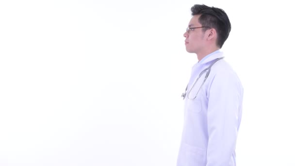 Profiel weergave van gelukkige jonge Aziatische man arts glimlachend met armen gekruist — Stockvideo