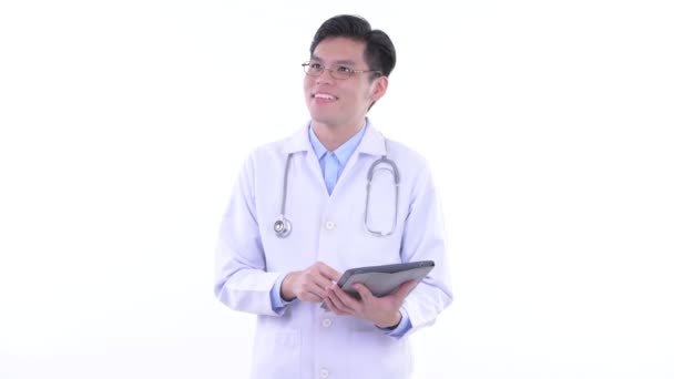 Feliz joven asiático hombre médico pensando mientras usa la tableta digital — Vídeo de stock