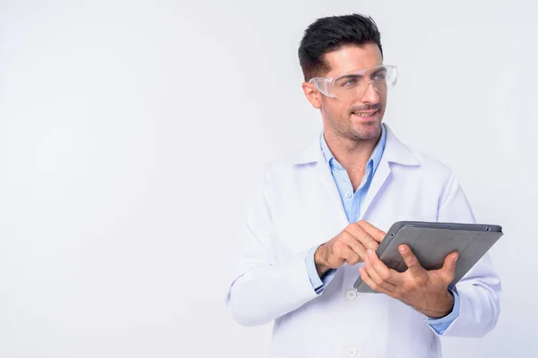 Junger gutaussehender Mann Arzt mit Schutzbrille denkt während er digitales Tablet benutzt — Stockfoto