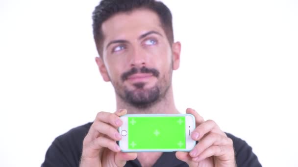 Faccia di felice giovane uomo bello barbuto pensando mentre mostra il telefono — Video Stock