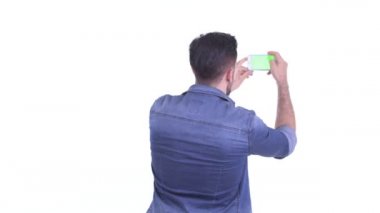 Genç sakallı hippi adam telefonla fotoğraf çekiyor.